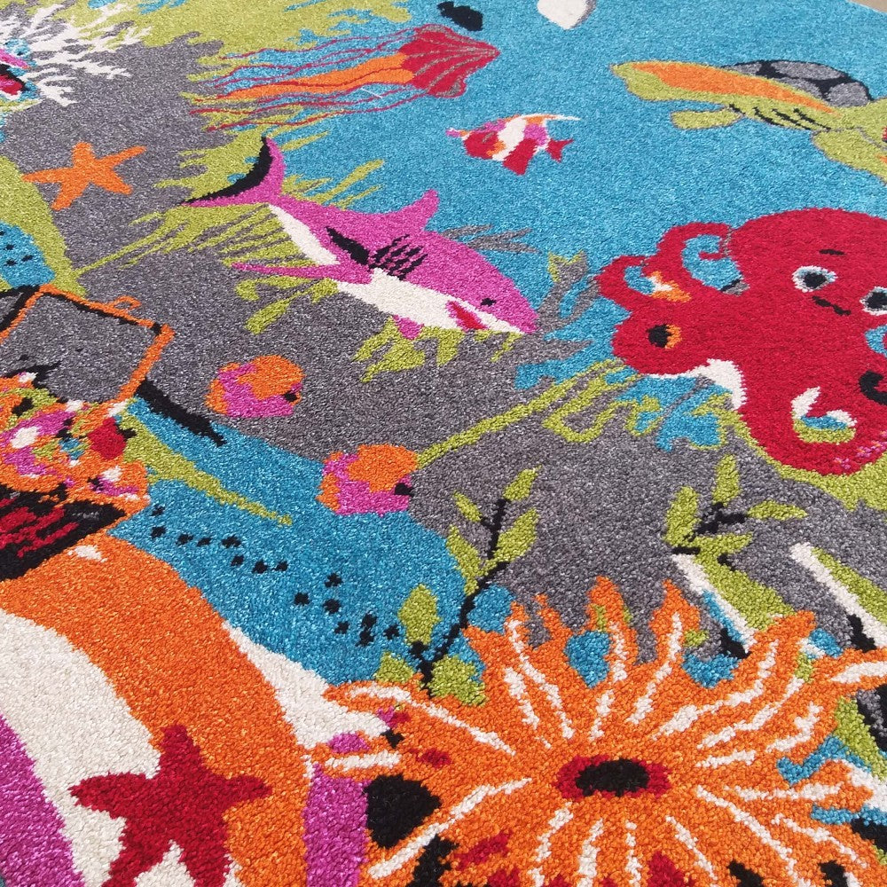 Tapis coloré à motifs marins avec requin rose, pieuvre rouge, poissons et coraux sur fond bleu et gris, présentant une texture épaisse