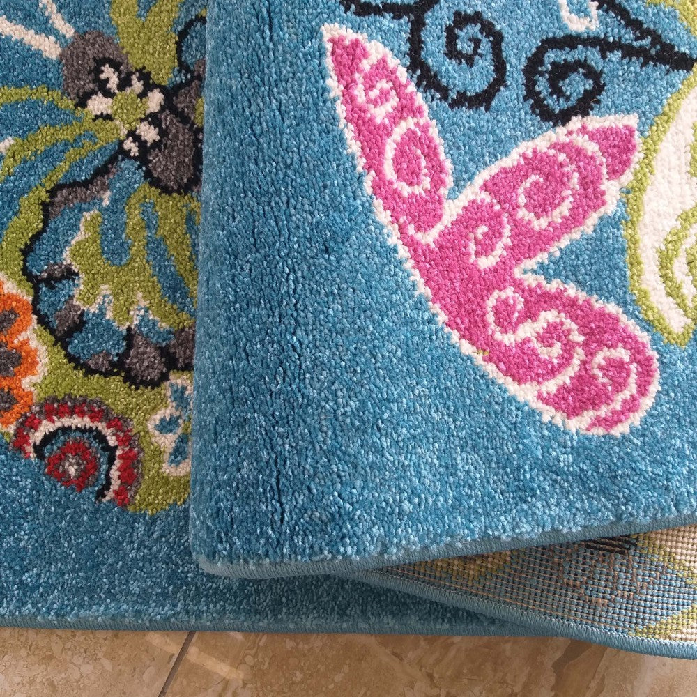 Gros plan sur un tapis à poils doux, plié pour révéler des motifs colorés de fleurs et papillons sur fond bleu turquoise