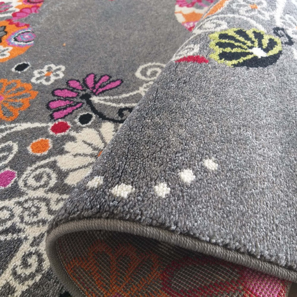 Tapis gris aux motifs floraux et cachemire multicolores, dont une partie est roulée, montrant sa surface en poils courts et son envers tissé aux teintes chaudes