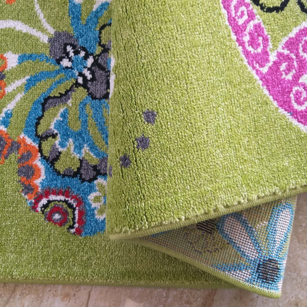 Tapis vert à poils courts avec des motifs floraux et cachemire multicolores (bleu, fuchsia, orange, gris). Une partie est roulée, laissant voir son envers tissé