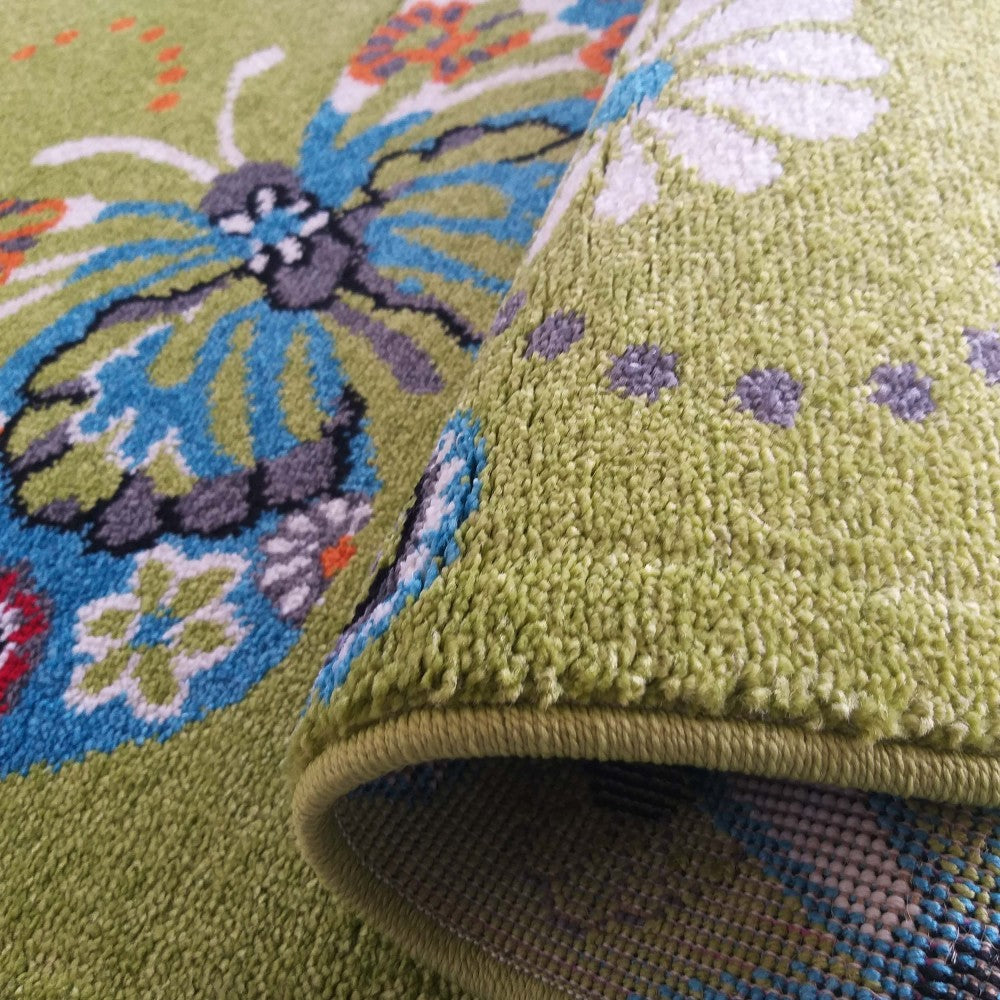 Tapis vert anis à motif grand papillon bleu, blanc et gris. Une partie est roulée, montrant la texture bouclée et des motifs floraux