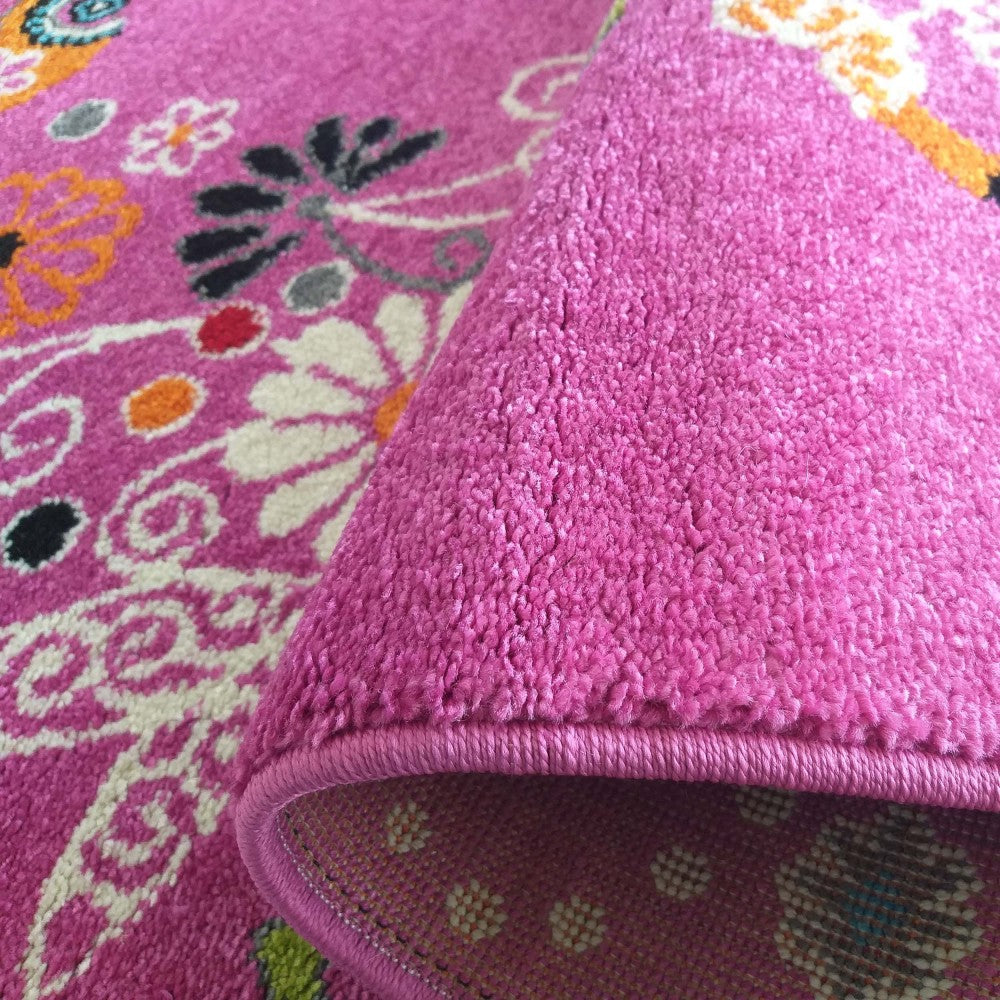 Tapis rose fuchsia à motifs floraux blancs, oranges et noirs. Partiellement enroulé, il révèle son envers rose clair à pois