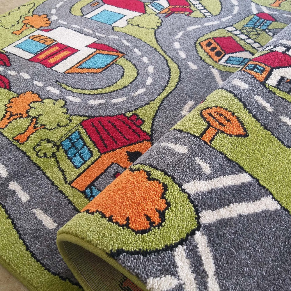 Tapis coloré représentant une ville avec des routes grises, des parcs verts et des maisons multicolores. Une partie du tapis est roulée