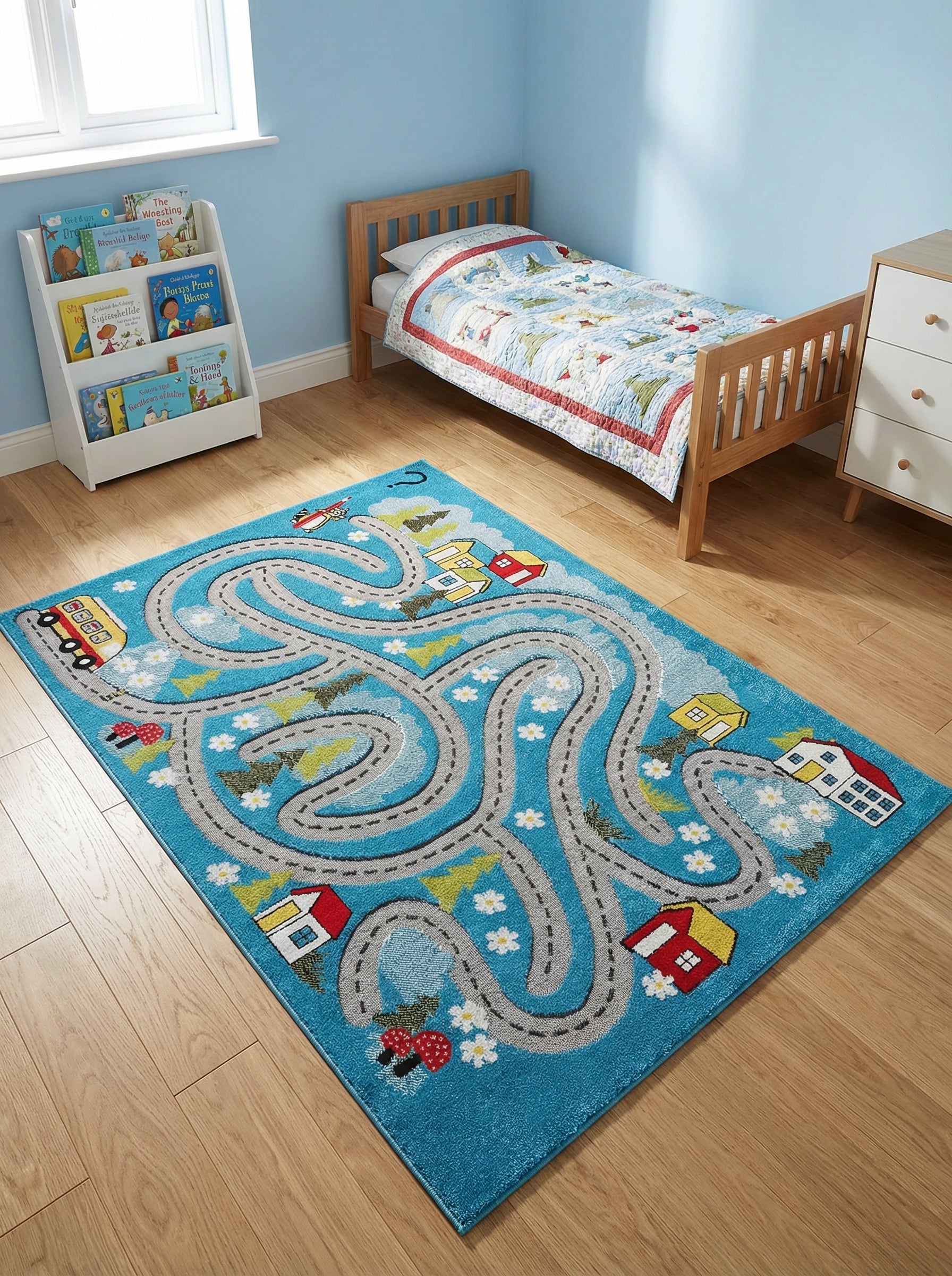 Tapis rectangulaire bleu ciel avec un circuit routier gris, des maisons colorées et des paysages, posé dans une chambre d'enfant