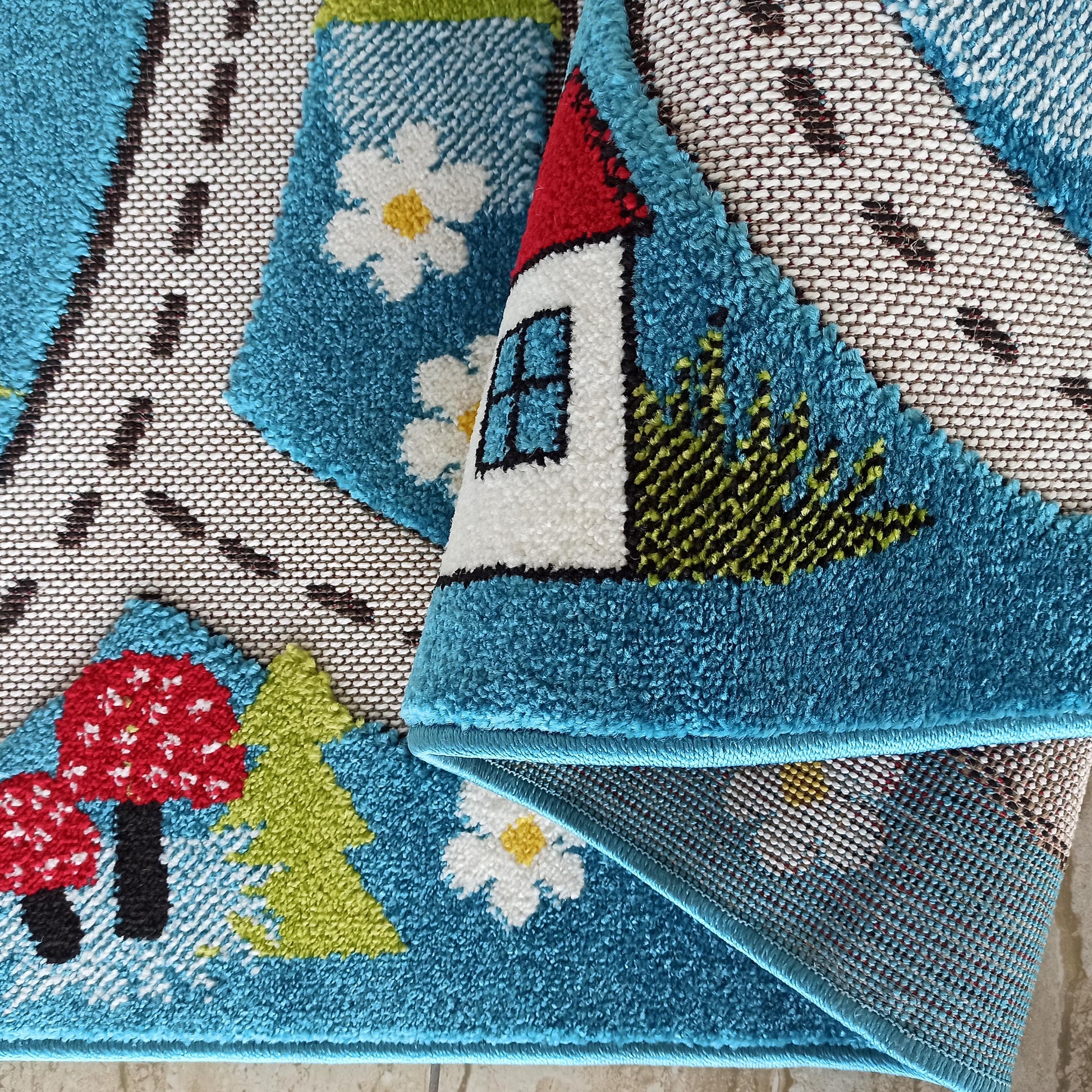 Tapis moelleux turquoise aux motifs enfantins: maison rouge et blanche, arbres verts, fleurs et champignons, avec une route