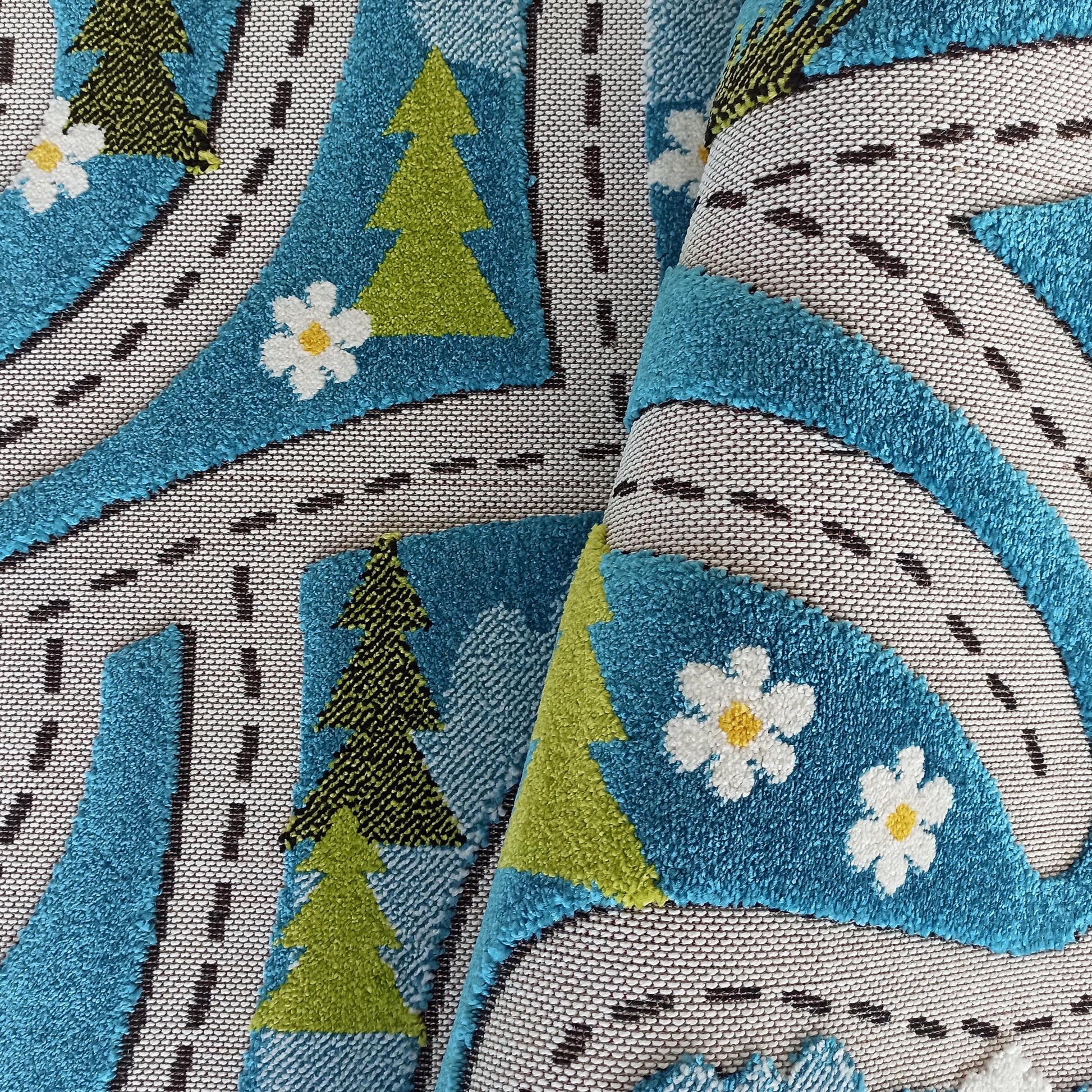 Tapis aux motifs de chemins gris tissés à traits noirs, d'arbres verts, de surfaces bleues bouclées et de fleurs blanches à cœur jaune