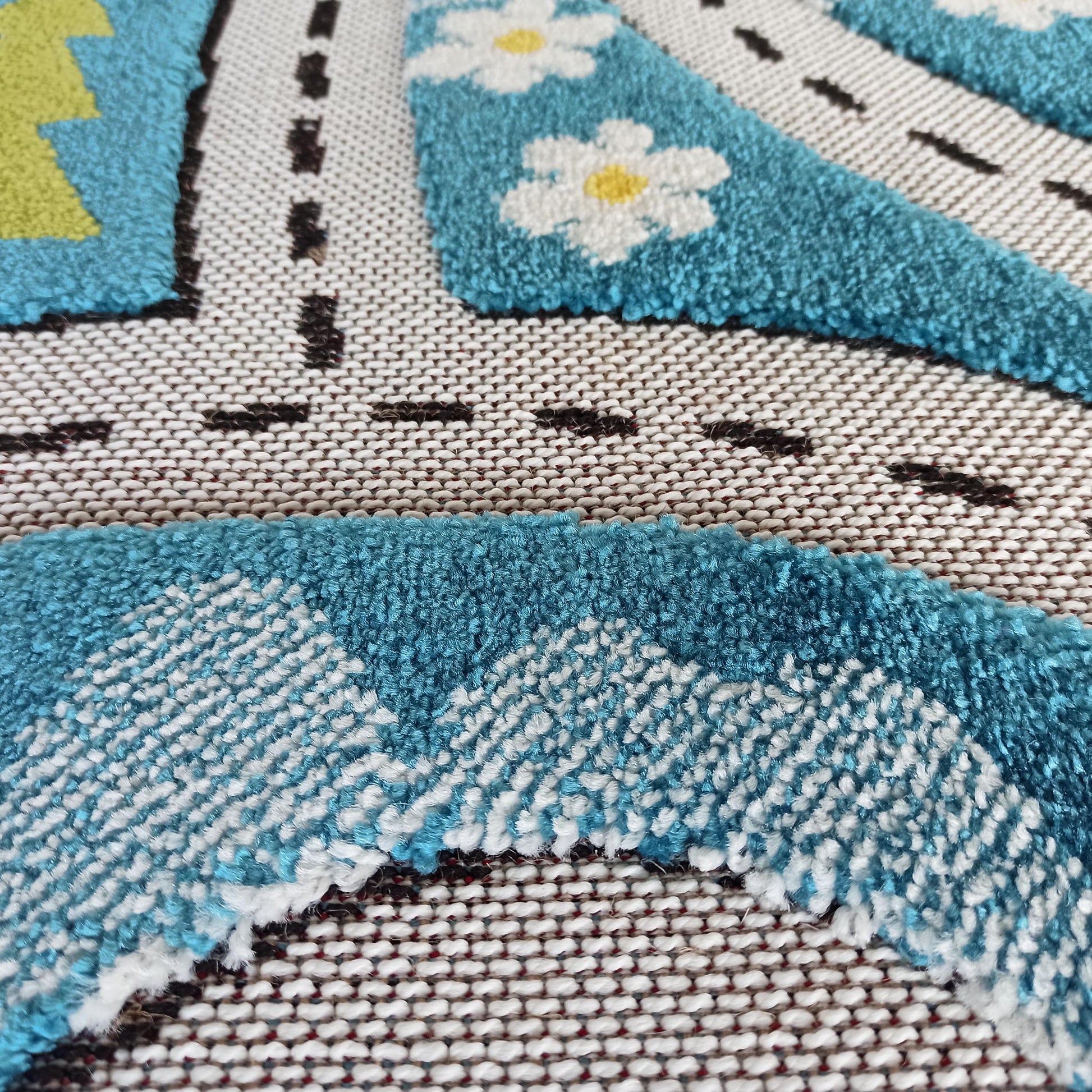 Tapis doux en gros plan, avec une route bleue bordée de blanc, des pointillés noirs et des fleurs blanches à cœur jaune
