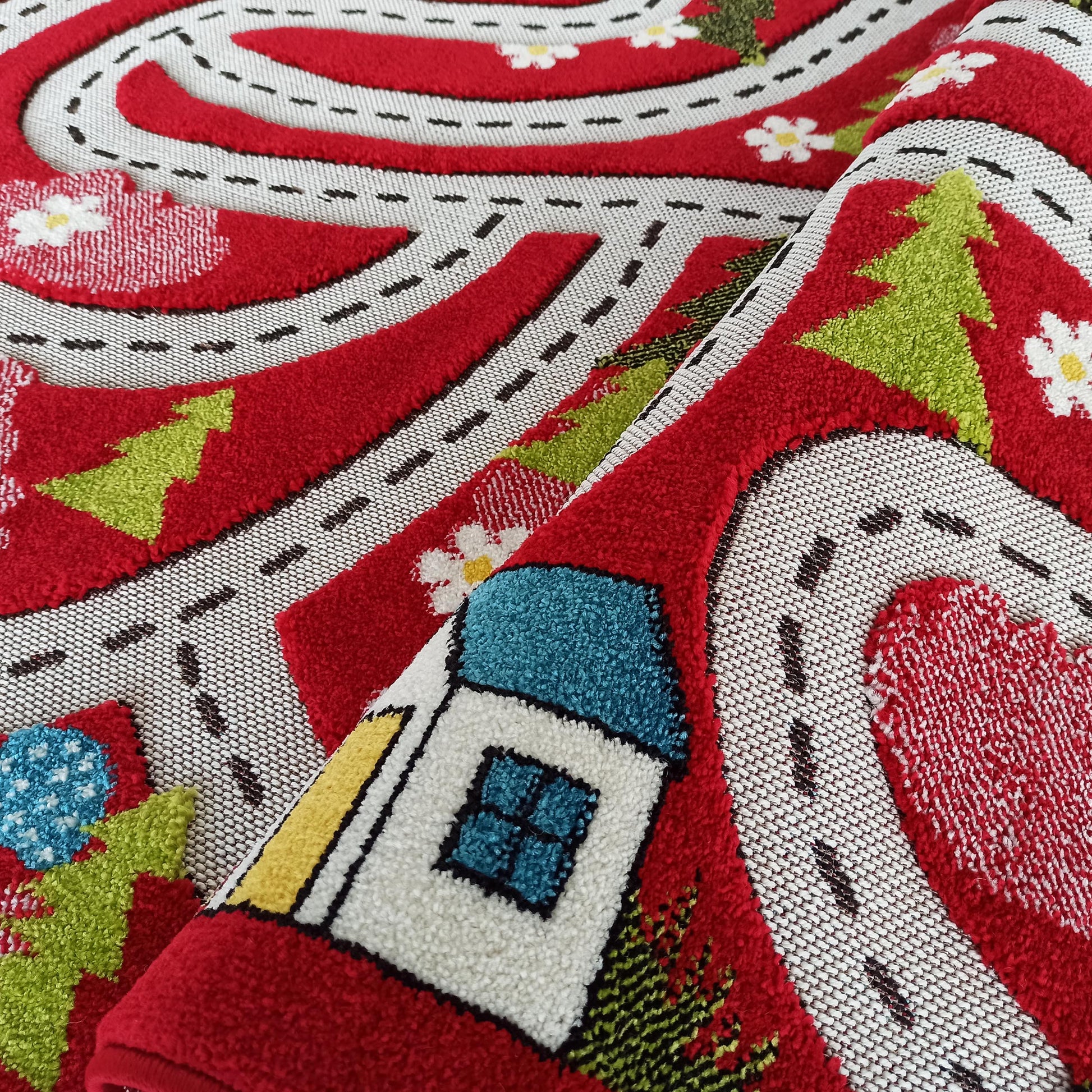 Tapis en textile bouclé rouge, blanc et multicolore, plié, avec un motif de routes, maison, arbres et fleurs