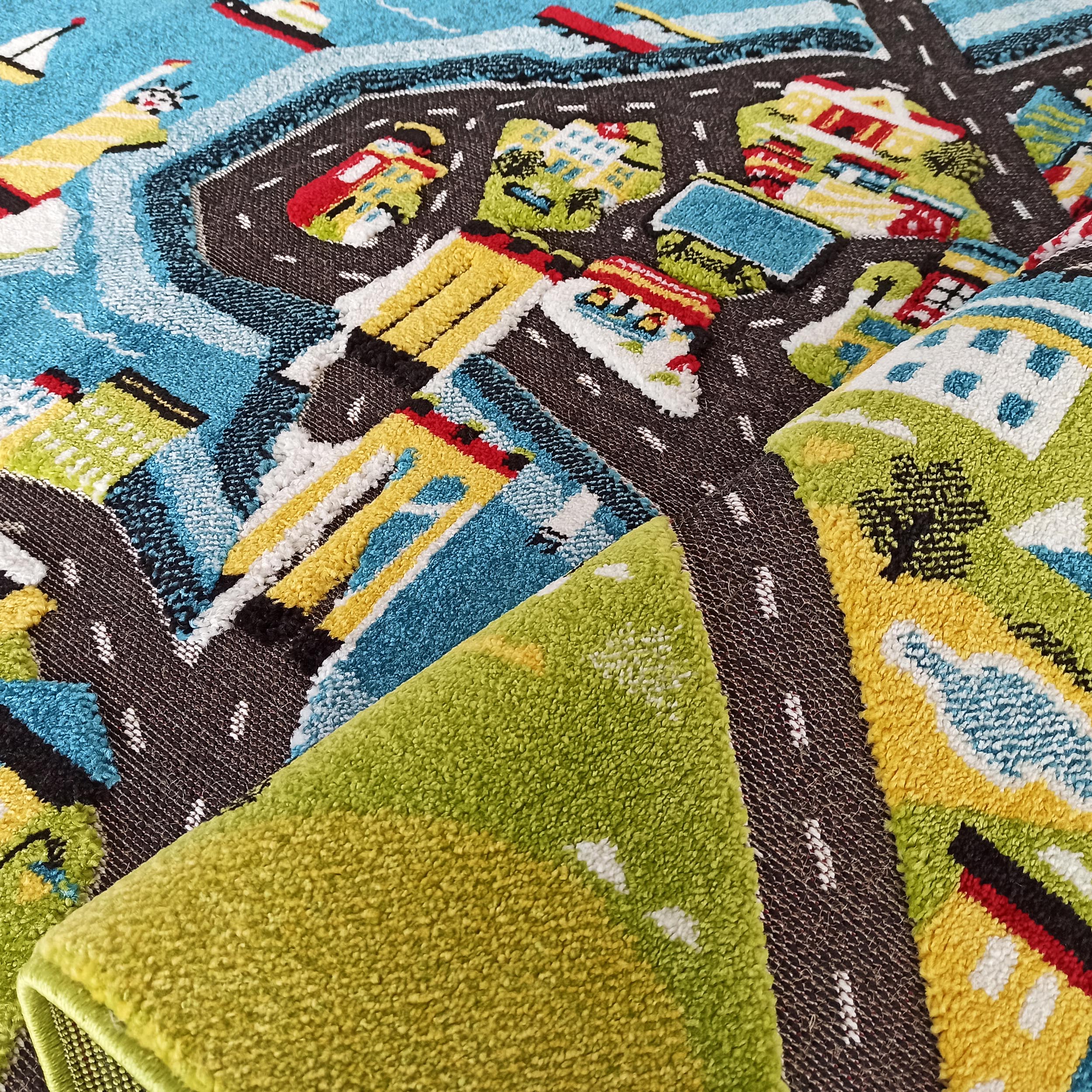 Tapis à motifs de ville colorés, partiellement enroulé. On distingue des routes grises, des maisons variées, des arbres verts et des plans d'eau bleus
