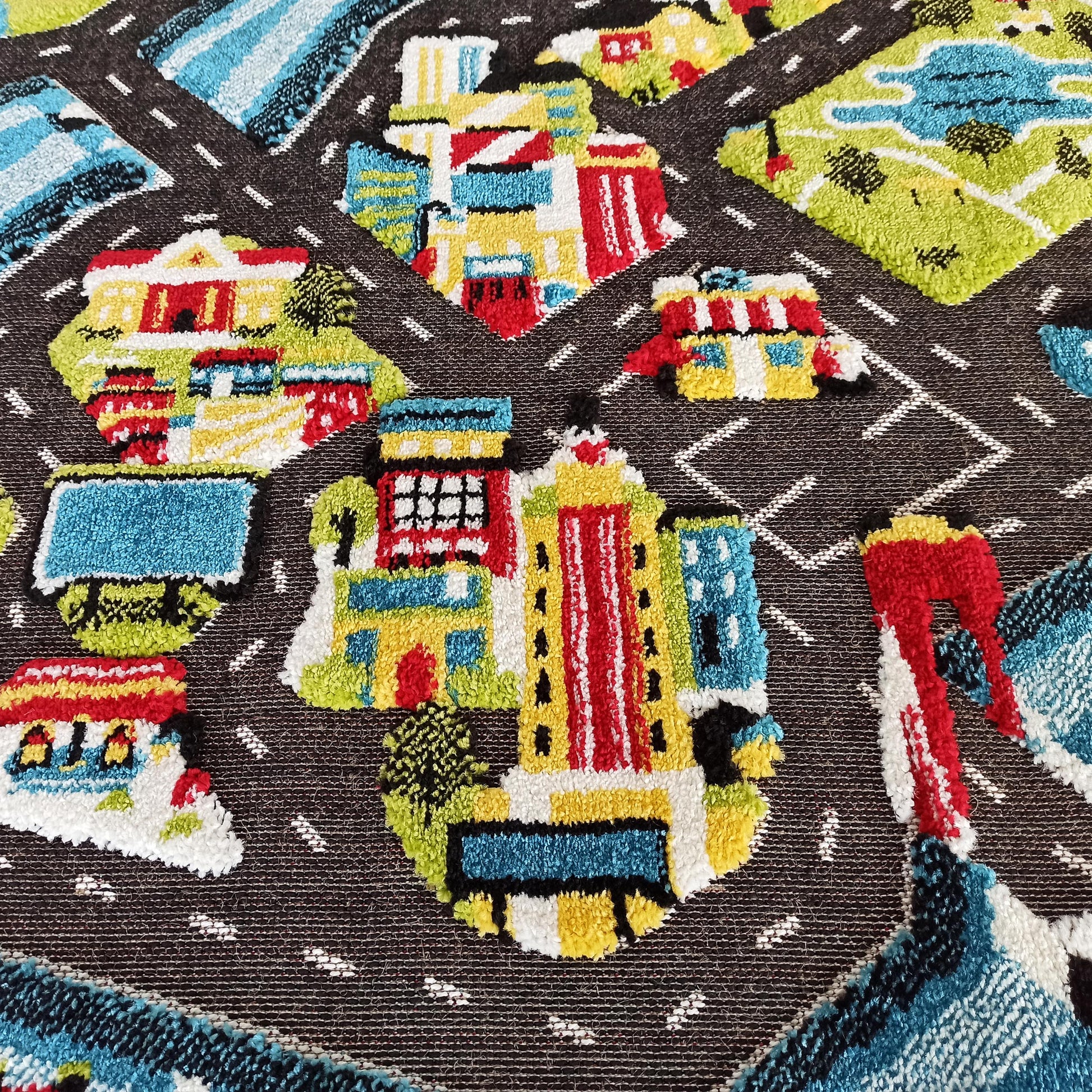 Tapis texturé doux aux motifs de ville colorés, avec des routes foncées et des bâtiments rouges, jaunes, bleus, verts et blancs en relief