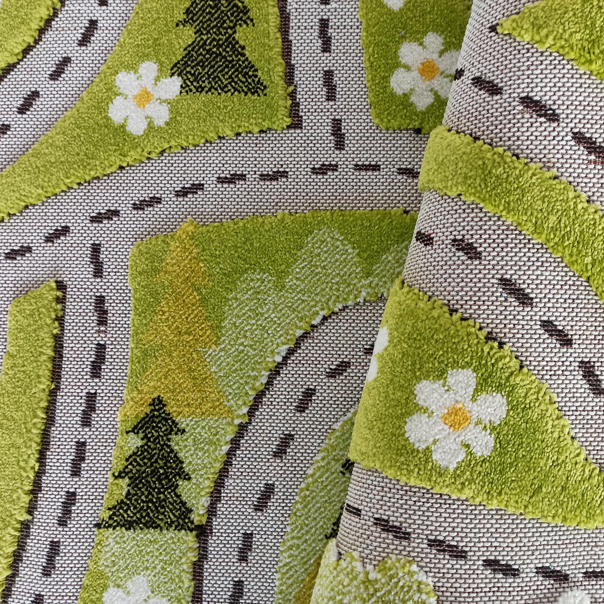 Tapis vert à la texture bouclée, orné de routes sombres, d'arbres et de fleurs blanches à cœur jaune, en partie enroulé