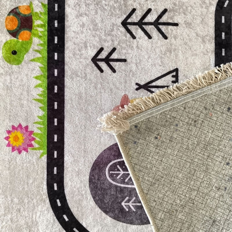 Tapis moelleux gris clair avec motifs de route noire, tortue verte, fleur rose et flèches, dont un coin relevé dévoile le dessous à texture tissée beige