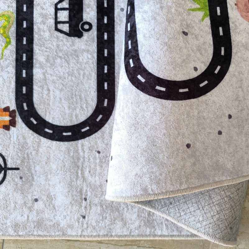Tapis gris clair texturé avec des routes noires et des motifs d'éléments colorés. Le coin relevé montre son dessous antidérapant