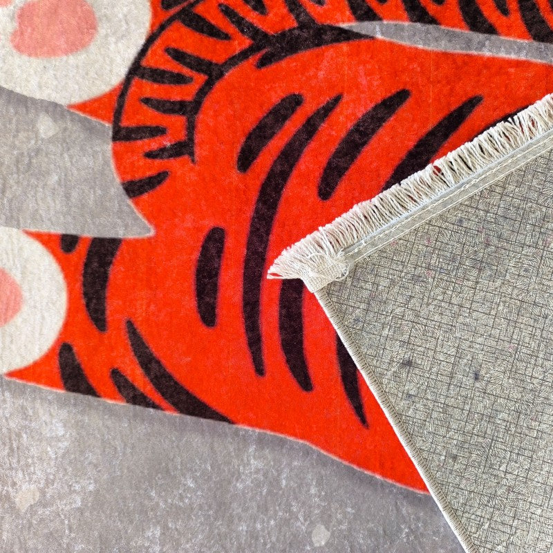 Tapis rouge vif à motifs de tigre noir, avec cercles blancs et roses sur fond gris, montrant son envers texturé beige et franges claires