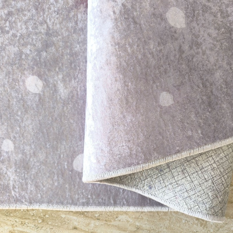 Tapis velouté gris-lavande à l'aspect vieilli, présentant des zones plus claires, son envers quadrillé étant visible