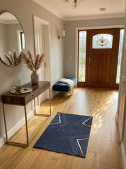 Tapis rectangulaire bleu marine à motifs géométriques dorés avec franges, posé sur un parquet clair dans une entrée