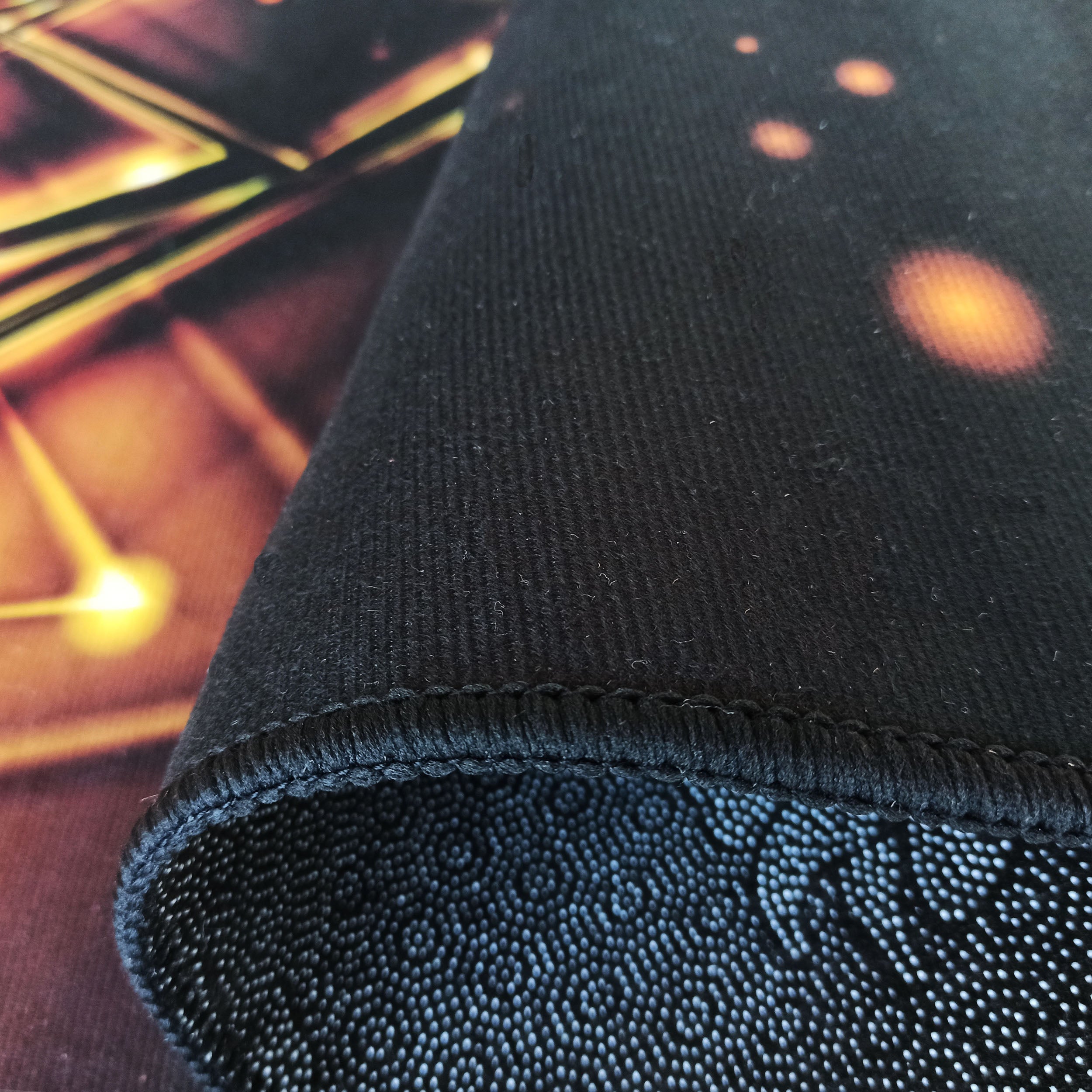 Gros plan d'un tapis. On voit son bord épais noir, une surface à motifs orange et jaune, et l'envers à picots antidérapants clairs