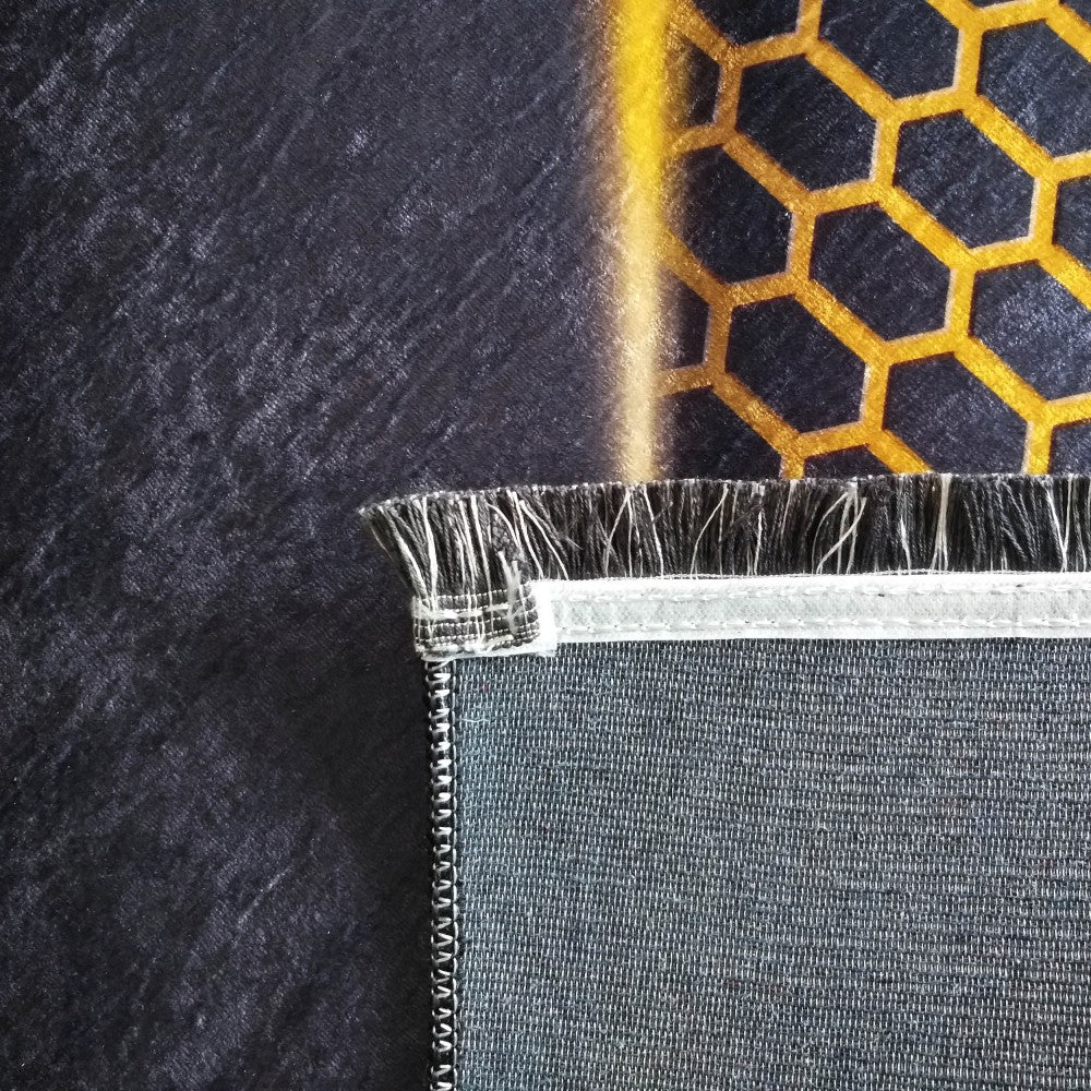 Tapis noir à texture douce avec motifs hexagonaux dorés et bande jaune. Le revers gris et le bord effiloché sont visibles