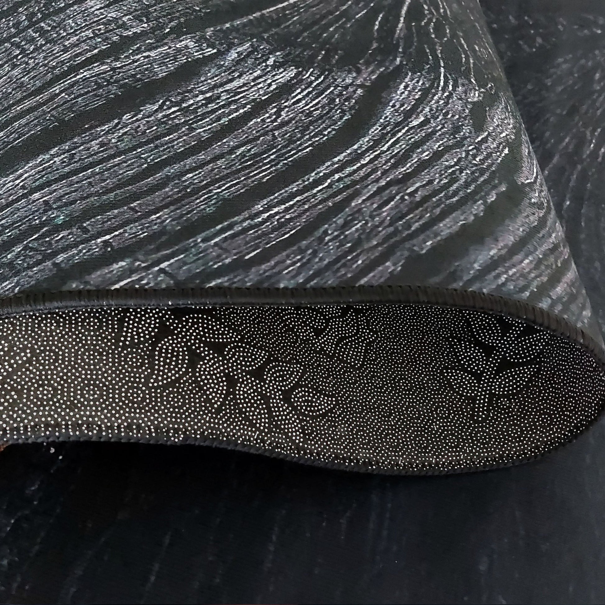 Tapis noir à texture striée gris argenté, l'envers visible présente un motif antidérapant de points blancs en spirales