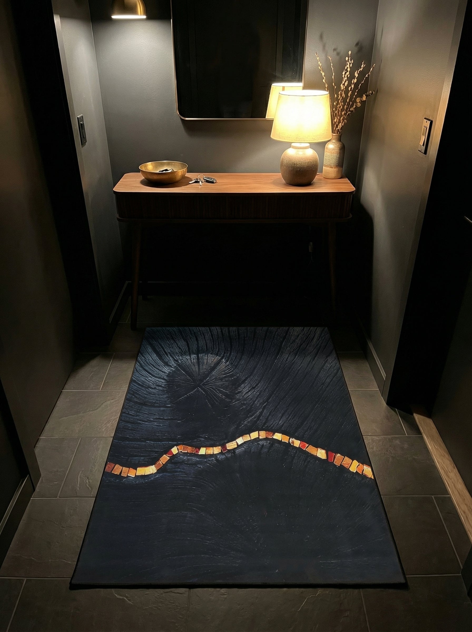 Grand tapis rectangulaire noir texturé, orné d'une bande ondulée lumineuse de tesselles aux couleurs chaudes (orange, jaune, rouge) dans une entrée