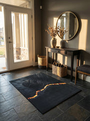 Tapis rectangulaire gris anthracite texturé de motifs circulaires, avec une bande ondulée de carreaux oranges et jaunes, dans une entrée