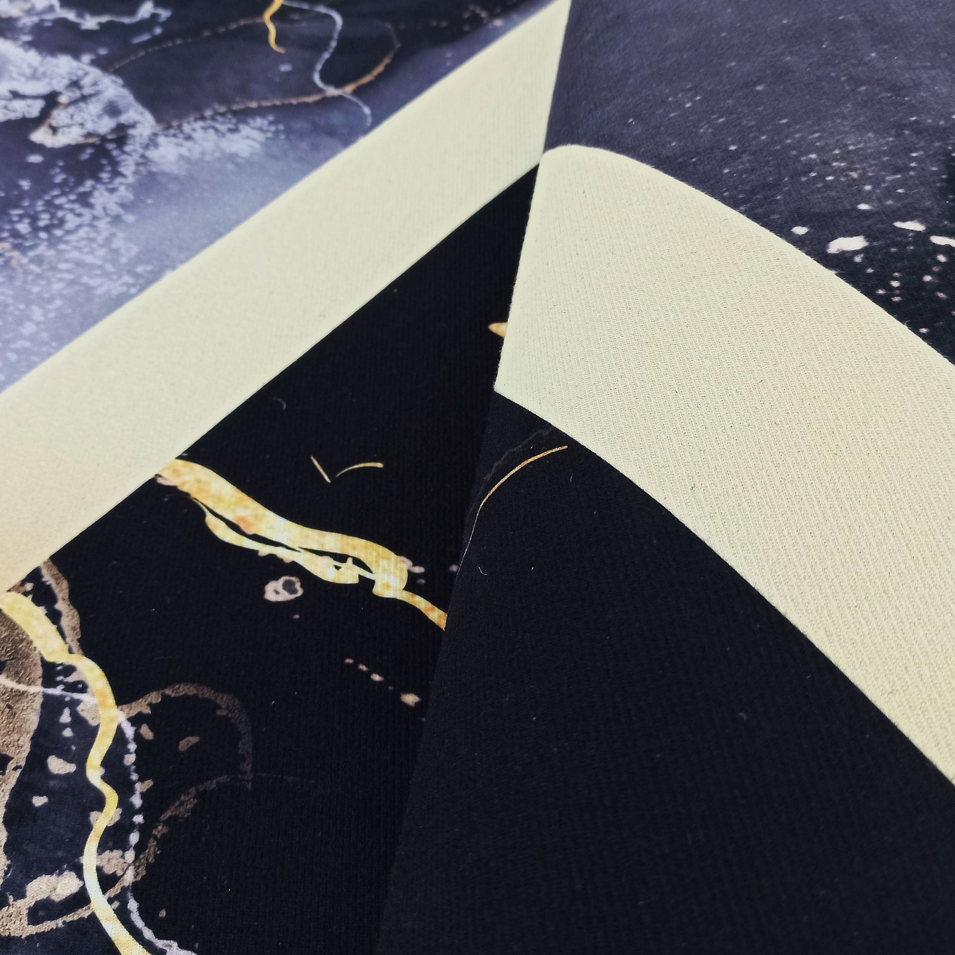 Tapis avec un motif abstrait marbré en bleu foncé, noir, blanc et doré, montrant son envers uni crème à la texture tissée
