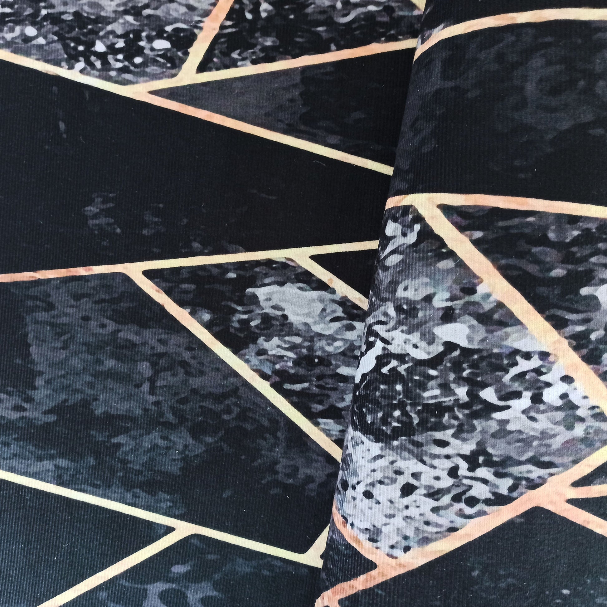Tapis avec motif géométrique de lignes dorées et texture marbrée grise sur fond noir, partiellement plié