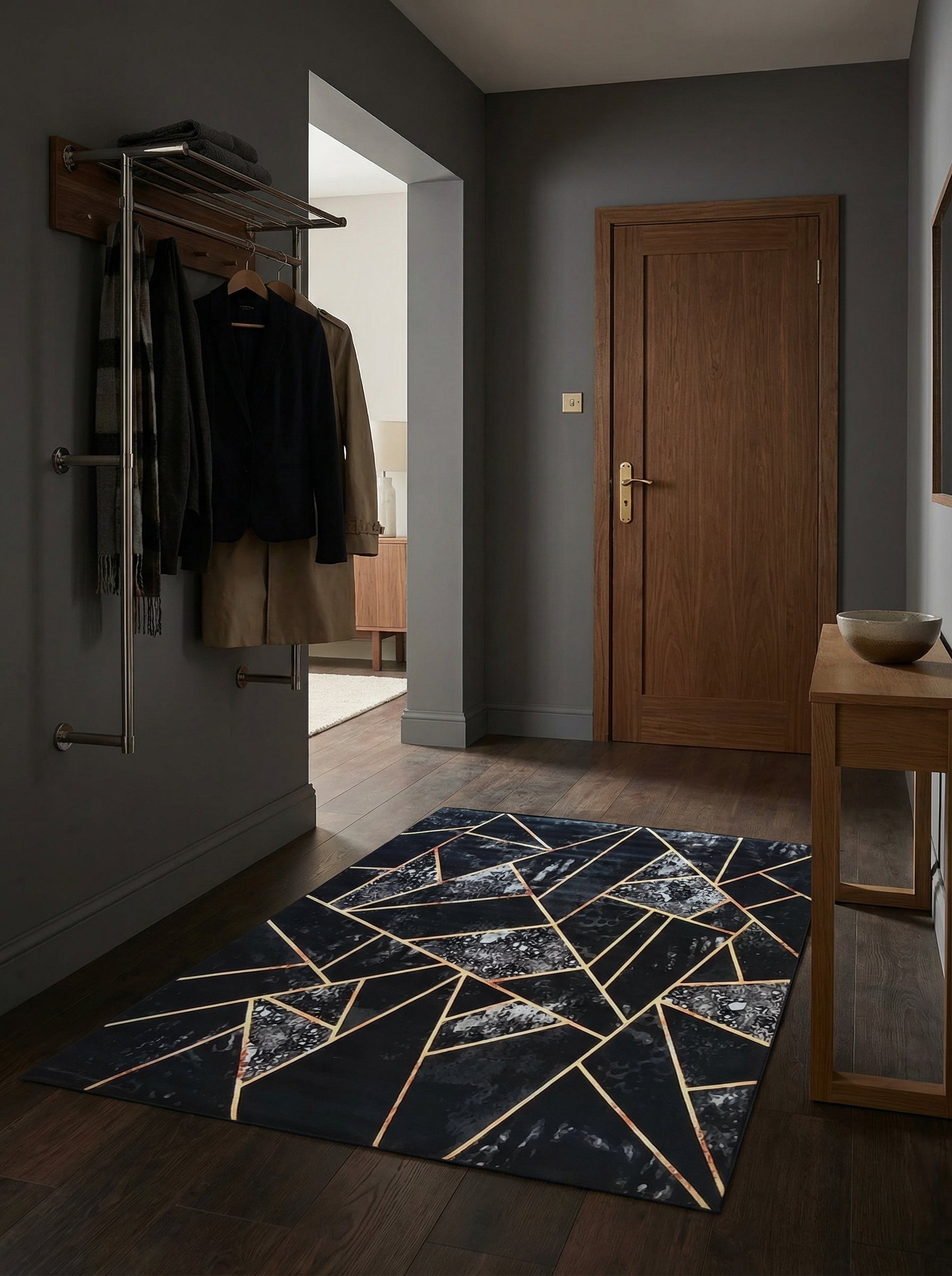 Tapis rectangulaire noir avec motifs géométriques dorés et zones marbrées grises, posé sur un parquet sombre dans une entrée