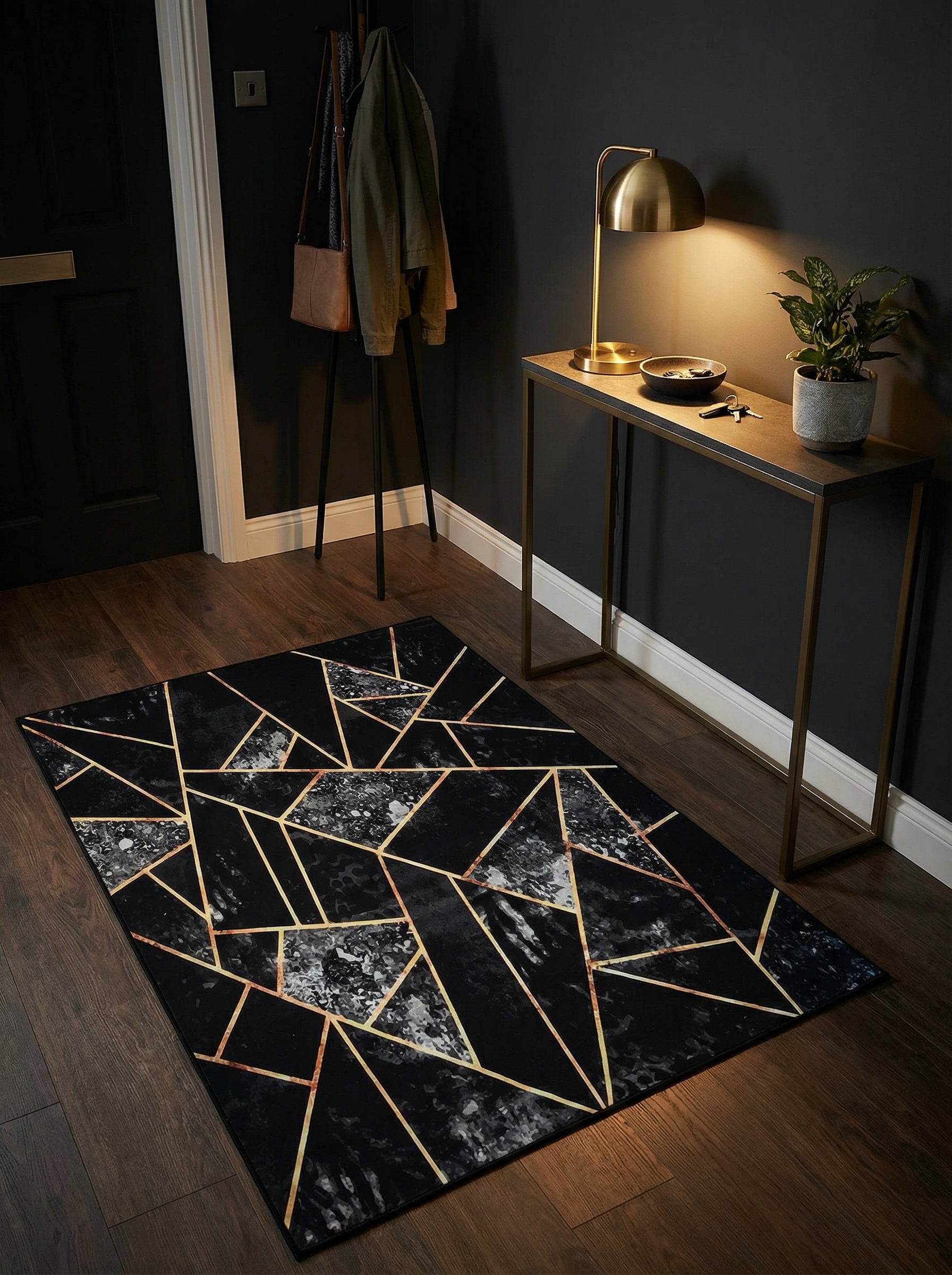 Tapis rectangulaire noir avec motifs géométriques dorés et incrustations marbrées grises, posé sur un parquet foncé dans une entrée moderne