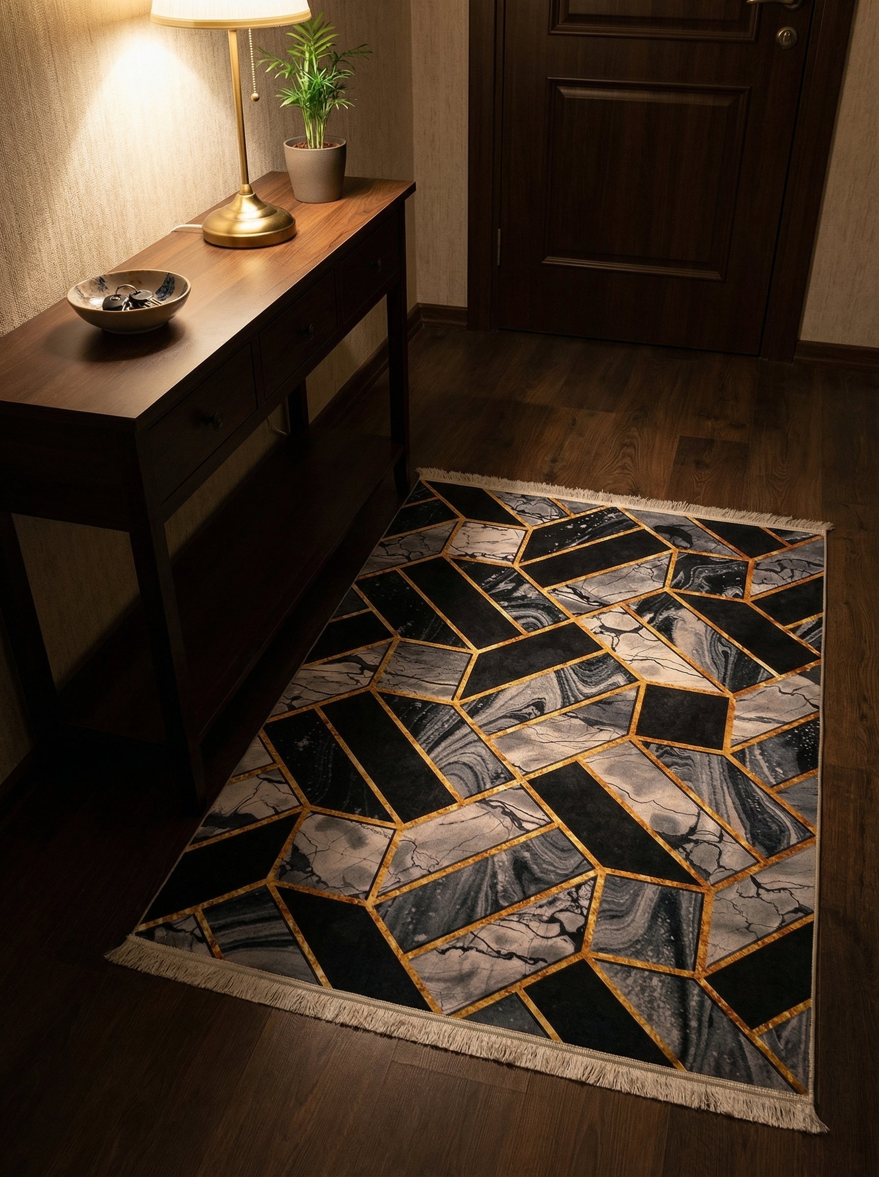 Tapis rectangulaire à motifs géométriques noirs, gris marbré et lignes dorées, avec franges, posé sur un parquet foncé dans une entrée
