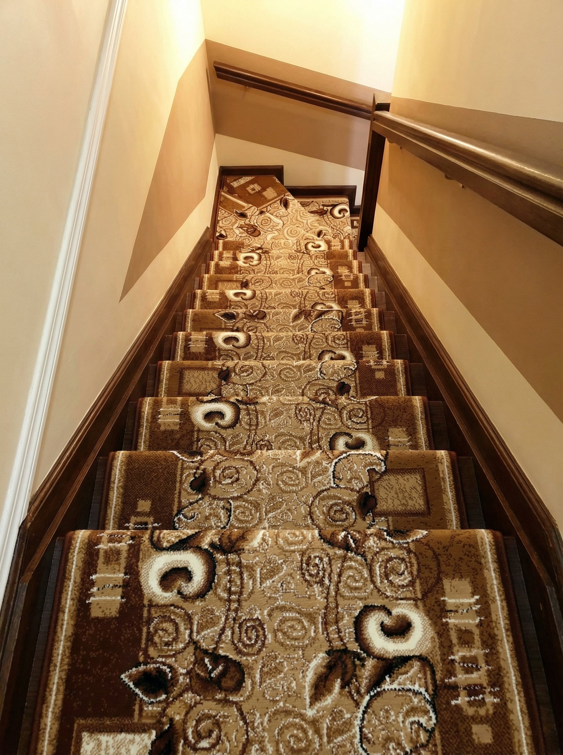 Tapis d'escalier beige et marron à motifs floraux et volutes, posé sur des marches en bois dans un couloir
