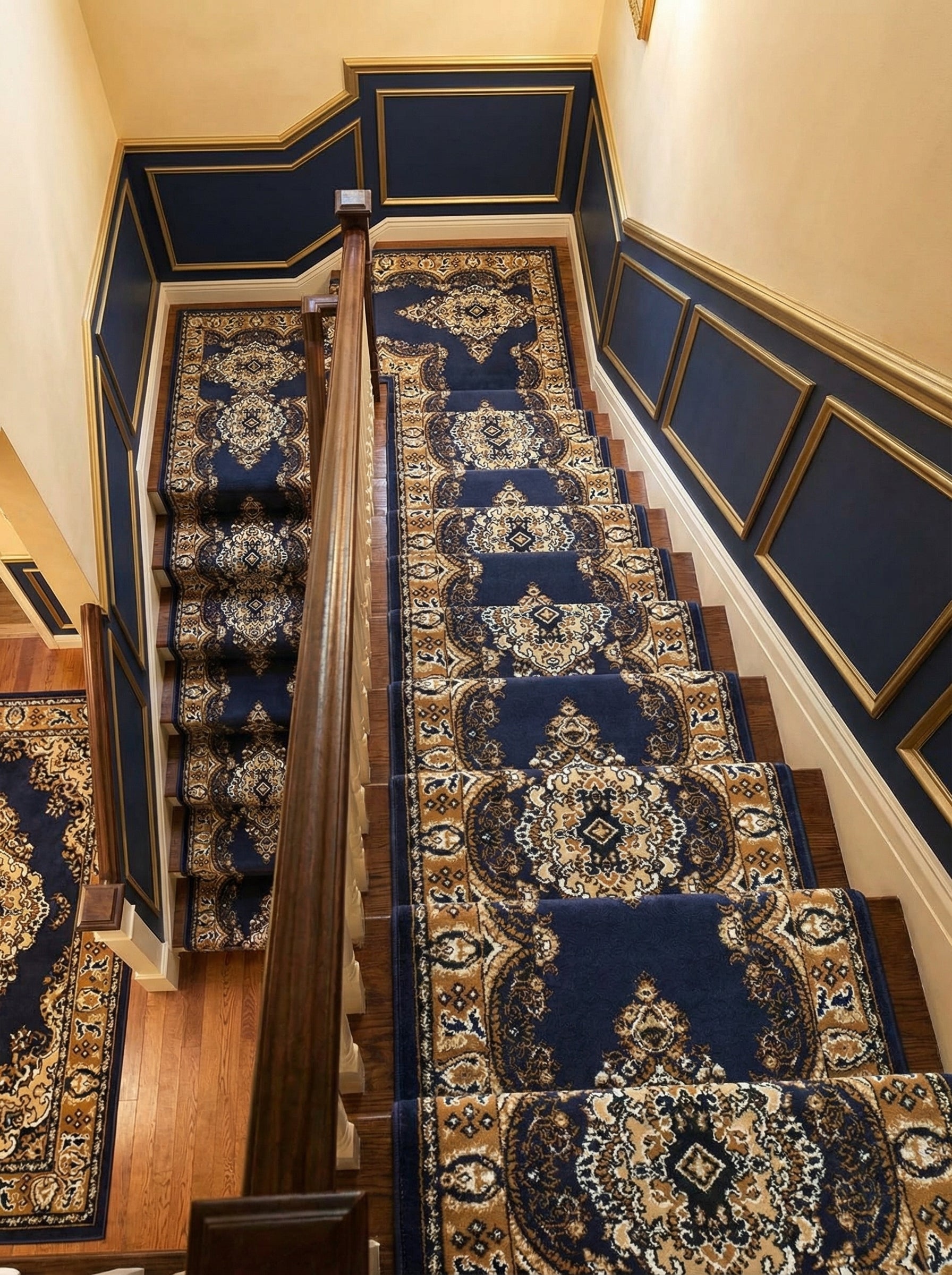 Tapis d'escalier bleu nuit à motifs floraux et médaillons dorés et crèmes, s'étendant dans une cage d'escalier richement décorée