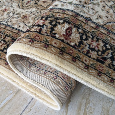 Tapis beige crème à motifs floraux et bordures noires et marron, partiellement roulé, à la texture douce et veloutée