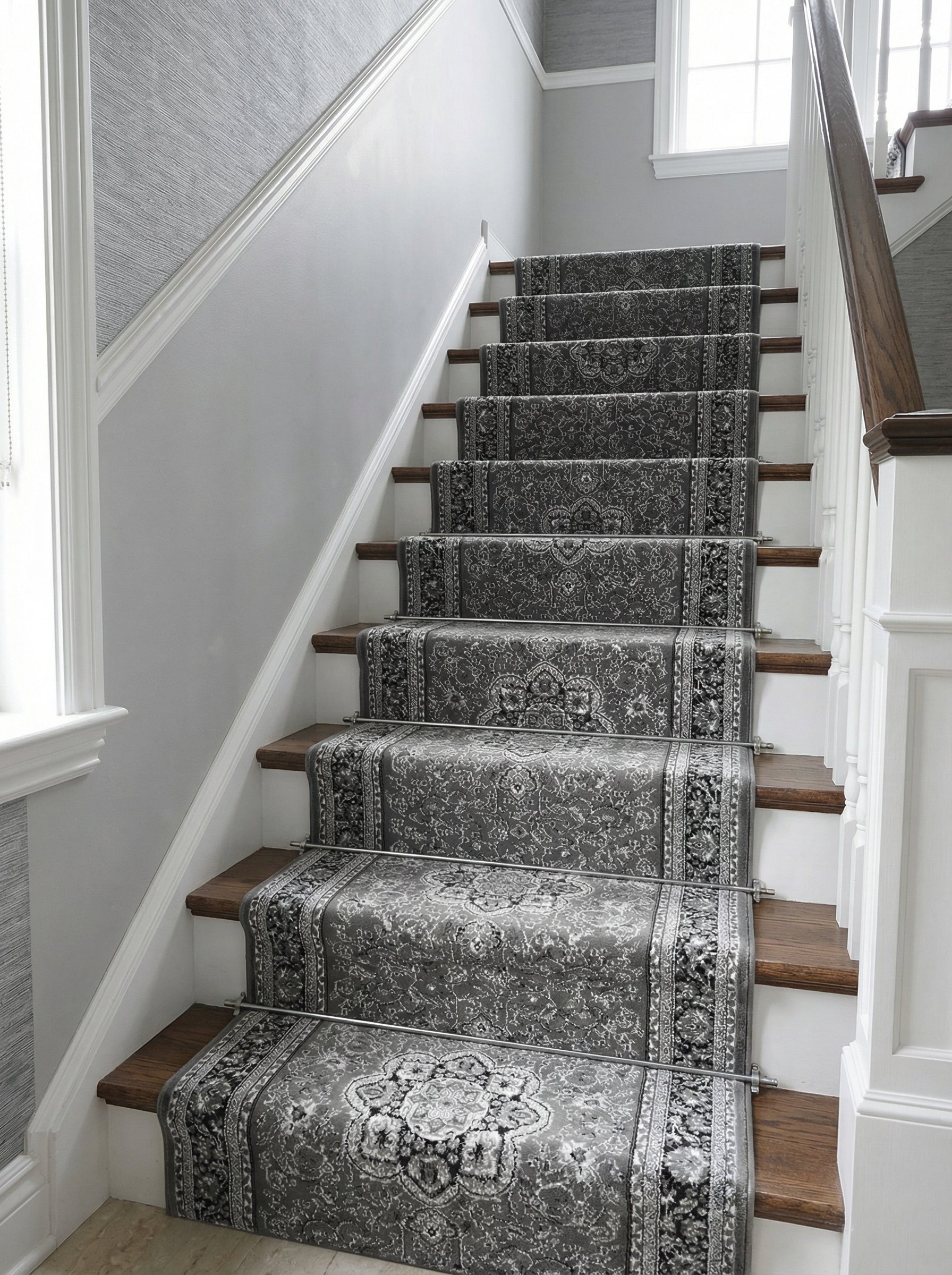Tapis d'escalier gris à motifs ornementaux de médaillons et bordures florales, maintenu par des barres métalliques, dans un hall élégant
