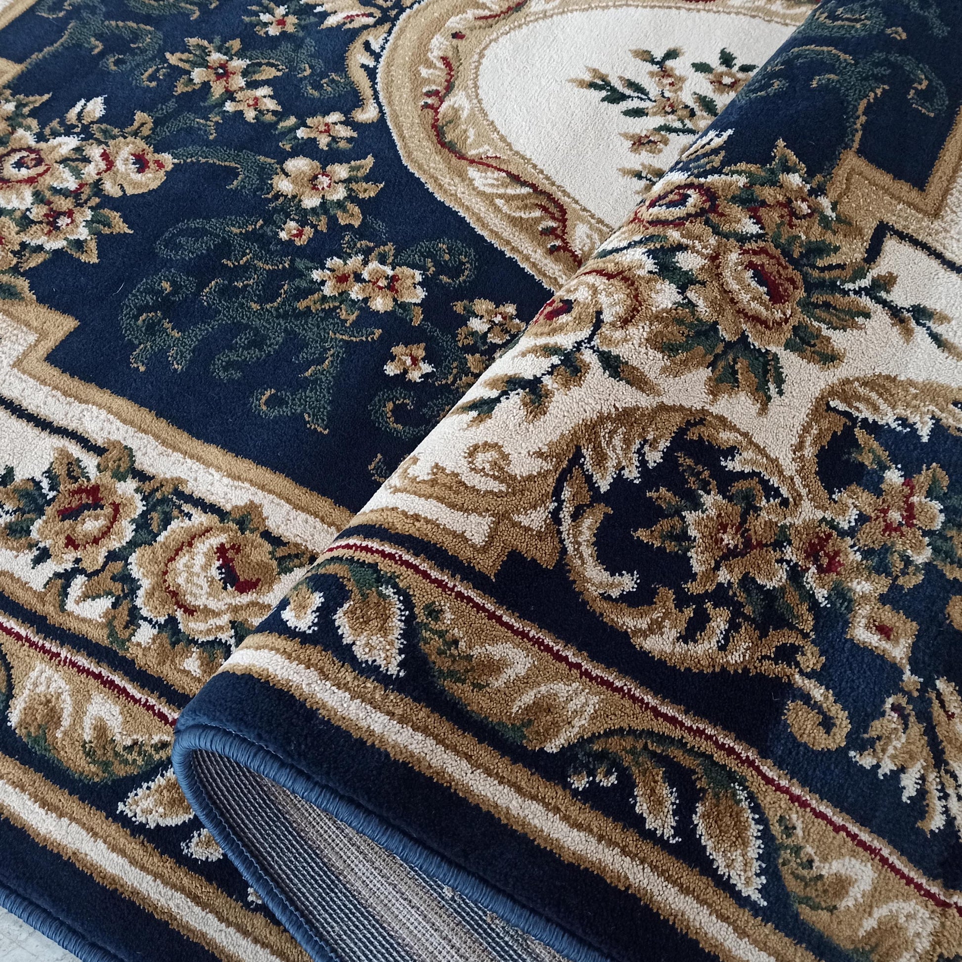 Tapis en velours bleu marine à motifs floraux et arabesques crème, beiges et verts, avec une section roulée