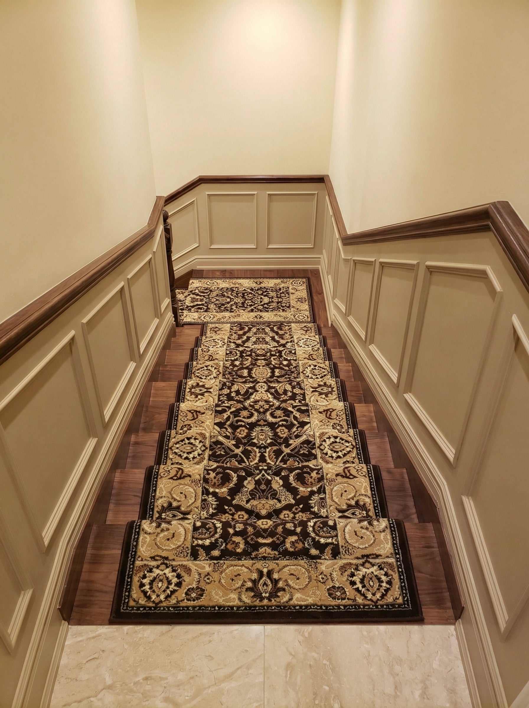Un tapis de couloir d'escalier marron foncé et beige à motifs floraux et arabesques, posé sur des marches en bois dans un hall élégant