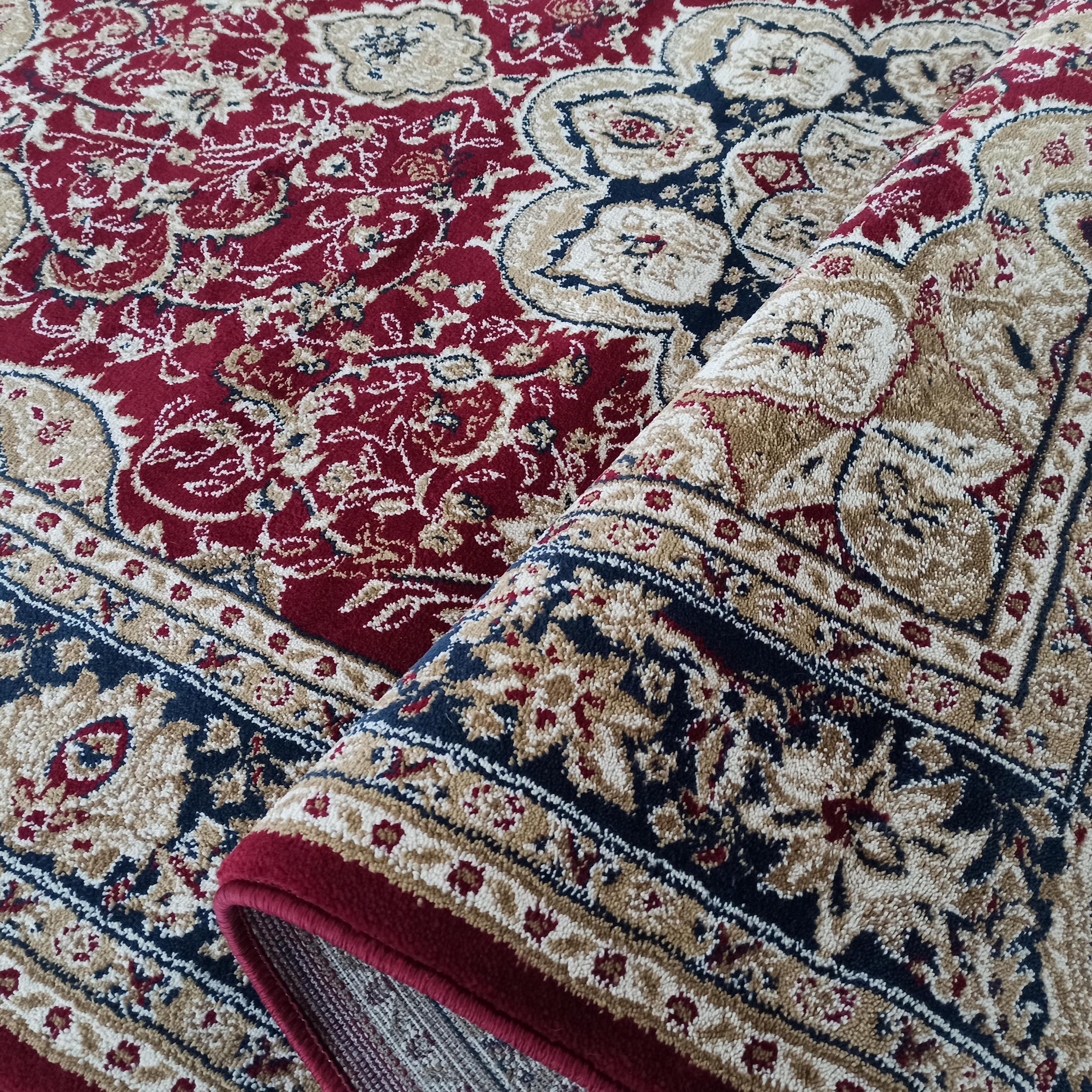 Tapis rouge bordeaux aux motifs floraux beiges, dorés et bleu marine, à la texture moelleuse, partiellement roulé
