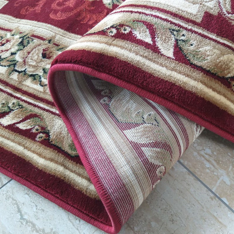 Tapis aux riches motifs floraux traditionnels rouges bordeaux, beiges et verts, partiellement roulé sur un carrelage clair