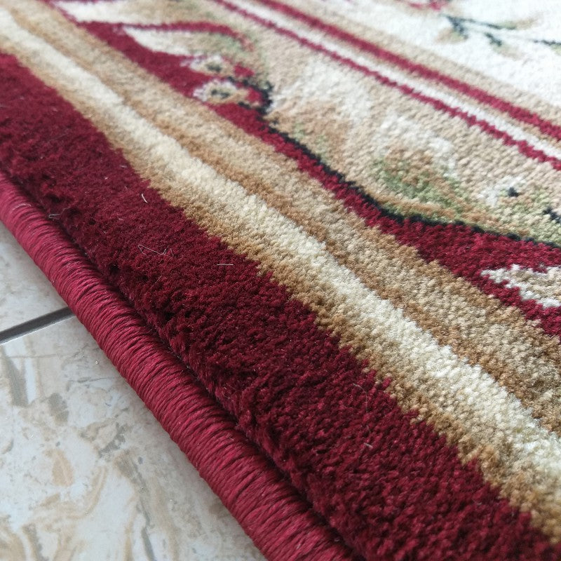 Tapis à poils courts orné de motifs floraux et de rayures rouges bordeaux, beiges et vertes. Ses bords sont visiblement ourlés de fil rouge