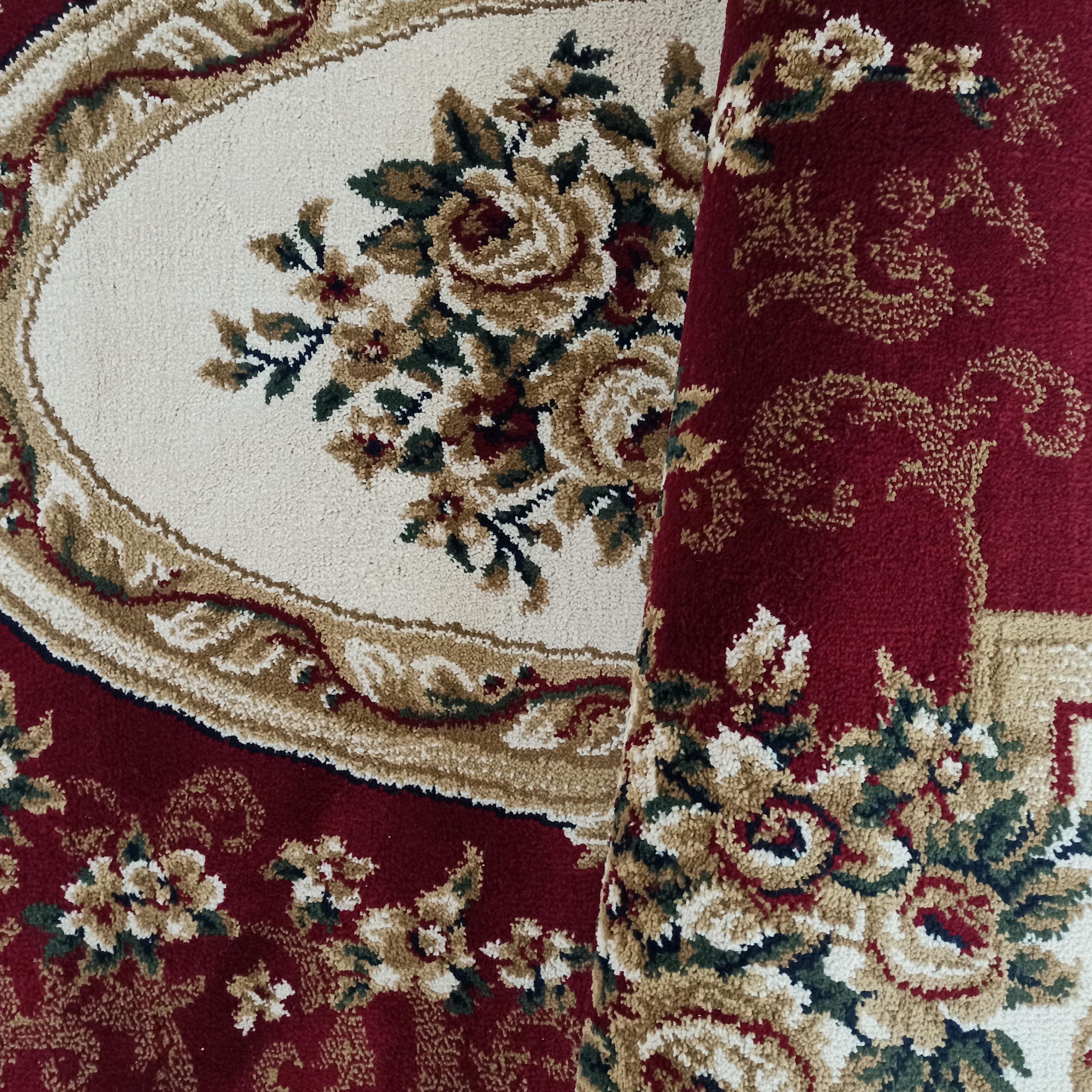 Tapis rouge bordeaux avec un médaillon central écru orné de roses beiges, rouges et vertes. Il est partiellement roulé