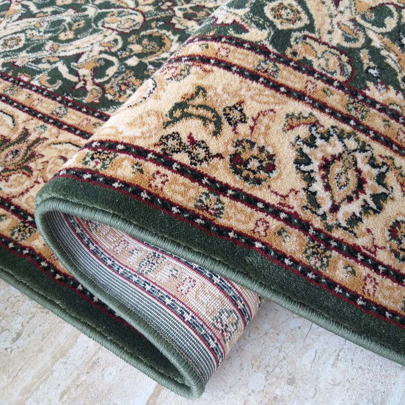 Tapis vert foncé et beige avec des motifs floraux ornementés. Une section est roulée, révélant la texture douce du tapis et son revers