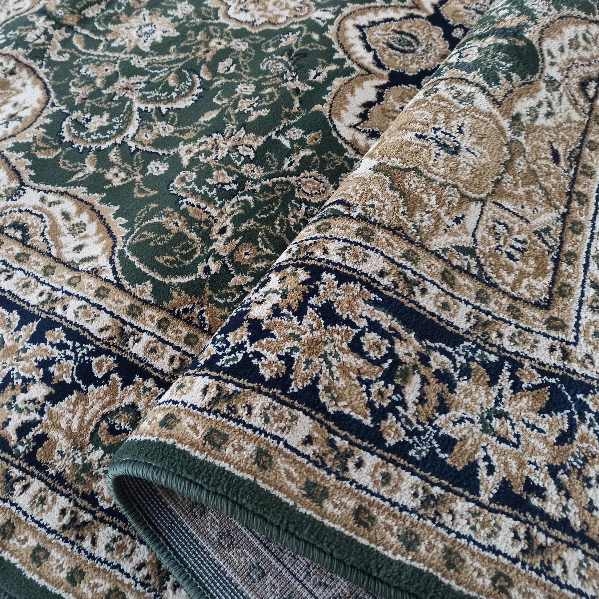 Tapis à motifs traditionnels verts, beiges et crème avec des accents bleu marine. Le tapis, à la texture dense, est visible partiellement roulé