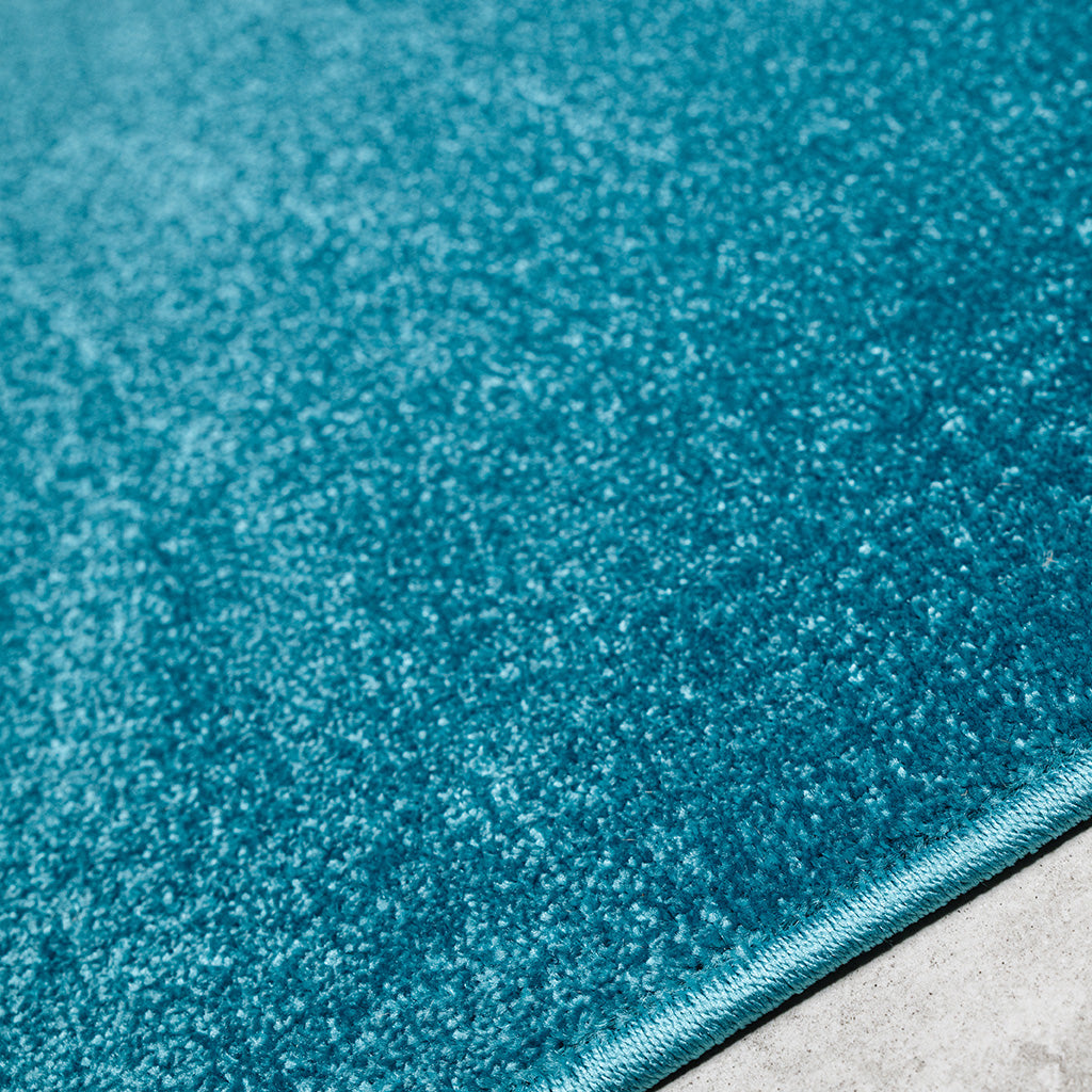 Tapis moelleux de couleur bleu-vert intense avec une texture à poils courts et une bordure cousue sur un fond clair