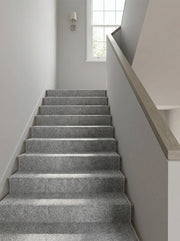 Tapis d'escalier gris chiné à motifs géométriques discrets, descendant le long d'une cage d'escalier lumineuse