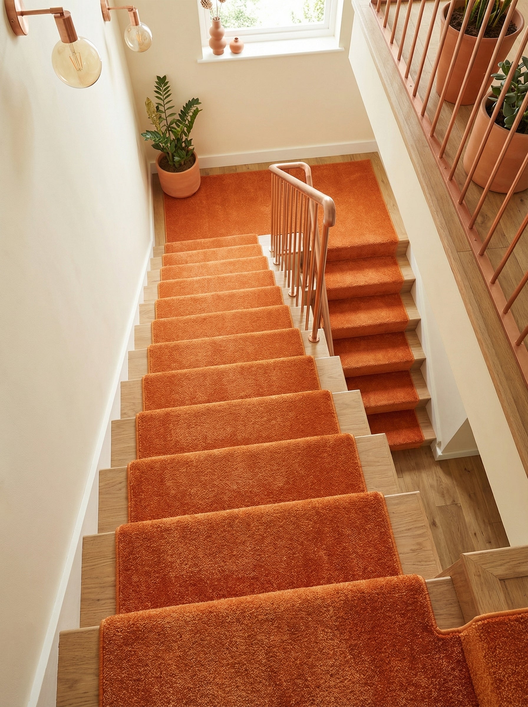 Tapis moelleux orange vif recouvrant un escalier en bois clair et son palier dans une entrée lumineuse