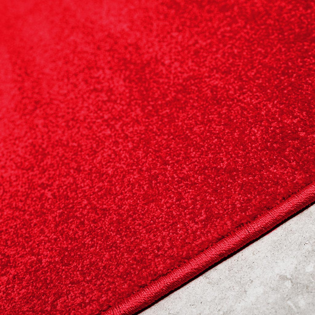 Détail d'un tapis textile rouge éclatant, présentant une surface texturée unie et une bordure finement cousue