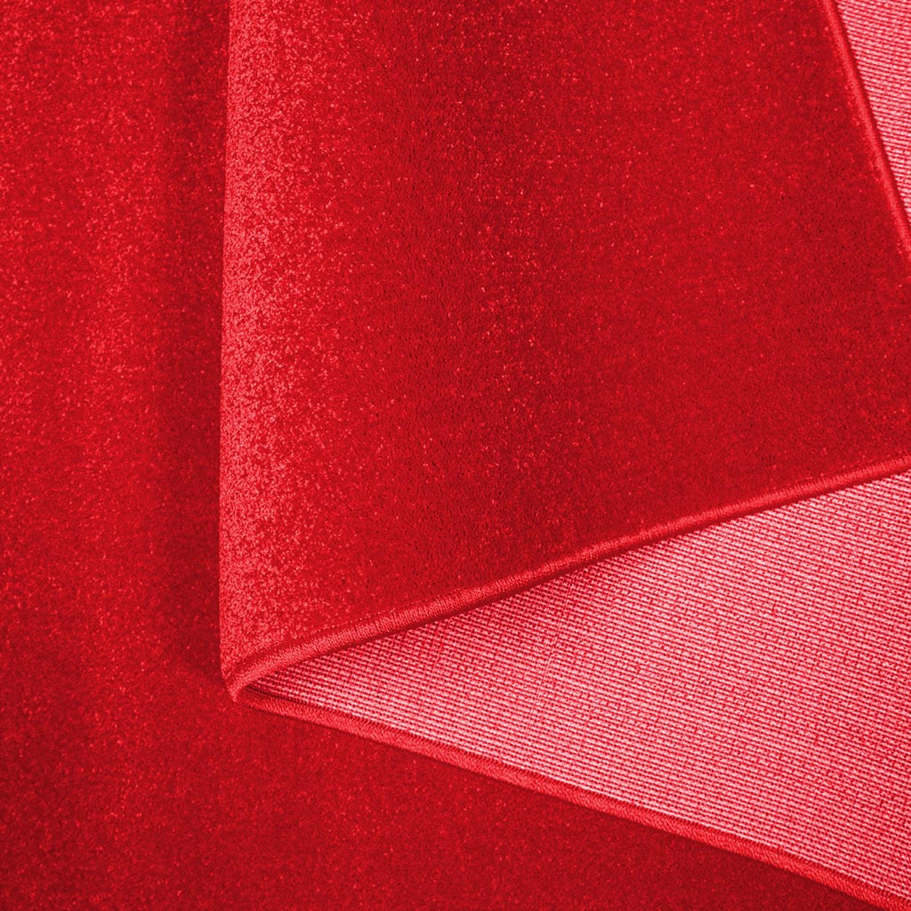 Tapis rouge intense à texture douce et uniforme, présentant un pli qui révèle son envers tissé et régulier