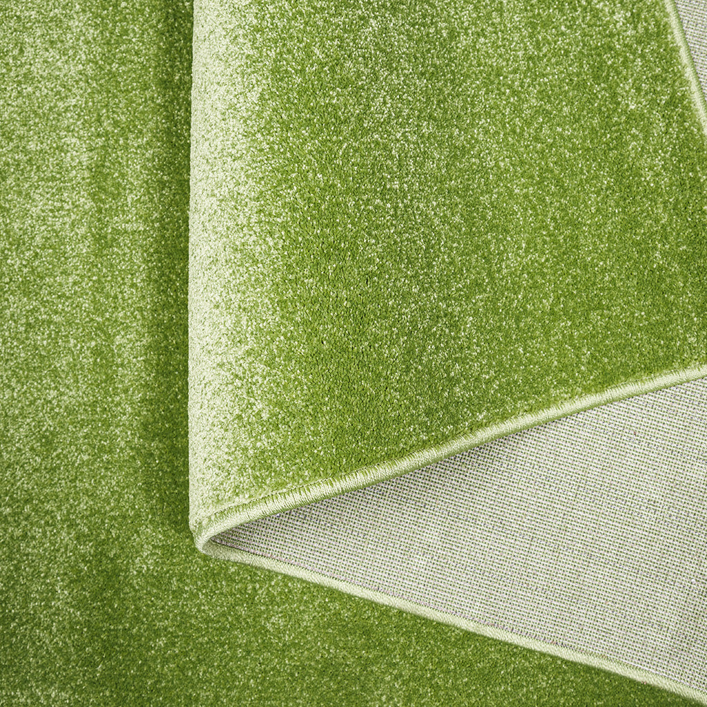 Tapis vert clair à la surface moelleuse et mouchetée, dont un coin est replié pour révéler son envers tissé gris