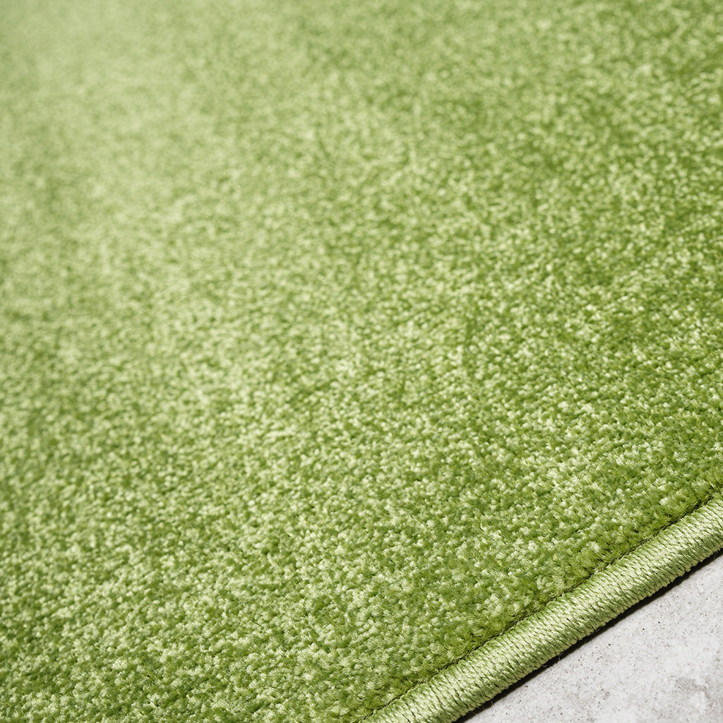 Gros plan d'un tapis vert pomme à la texture douce et moelleuse, avec un bord surpiqué. Il repose sur un sol gris