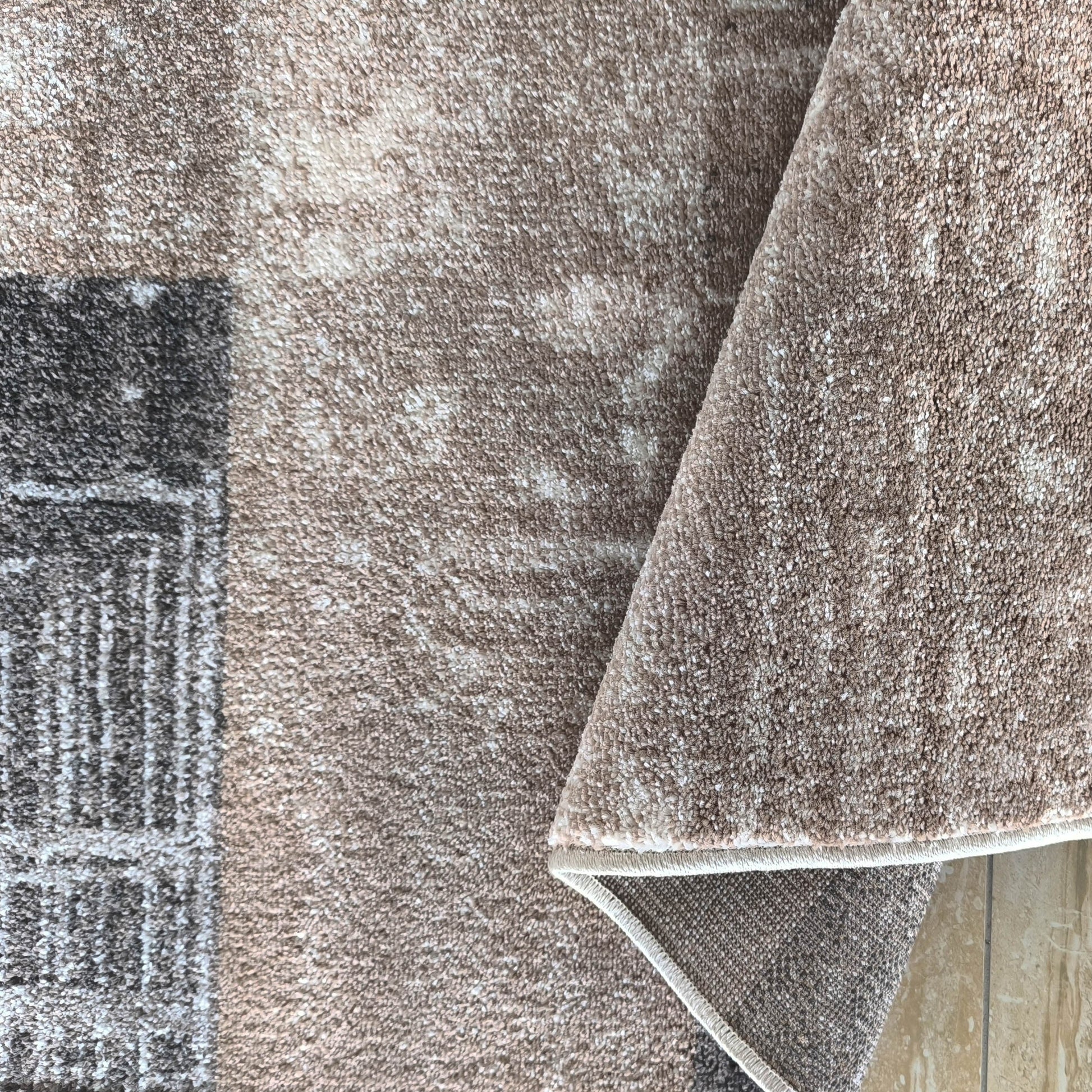 Tapis texturé beige et blanc à motifs rectangulaires gris foncé, replié sur son envers tissé et le carrelage beige